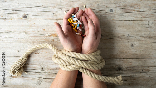 Fotografía Hands of man are tied with a rope and in his hands he holds many different pills