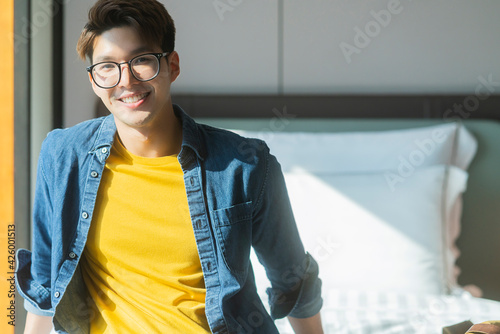 attractive asian mature adult male traveller wear casual cloth and glassses sit smiling relax on bed at hotel travel vacation ideas concecpt photo