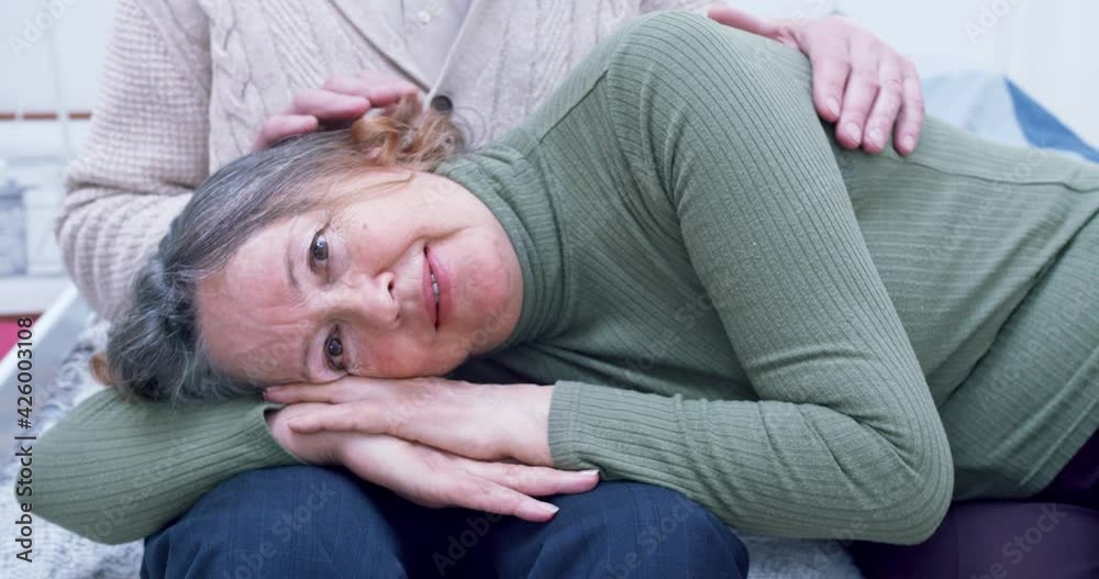 portrait of an elderly woman who lies on her husband's lap and looks into the camera. husband strokes his head, hair and back showing attention portrait of an elderly woman who lies on her husband's lap and looks into the camera. husband strokes his head, hair and back showing attention
