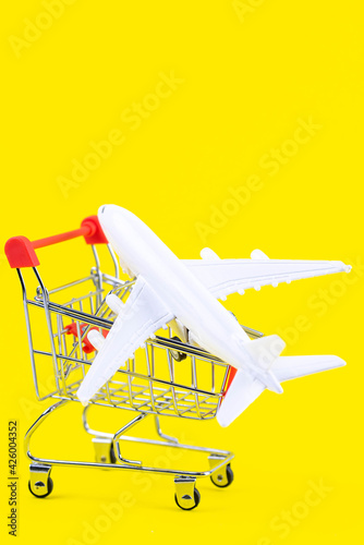 Flight sale concept. Vacation travel tour. Tourism opening. Plane in a shopping cart on trendy yellow background. Cheap flights.