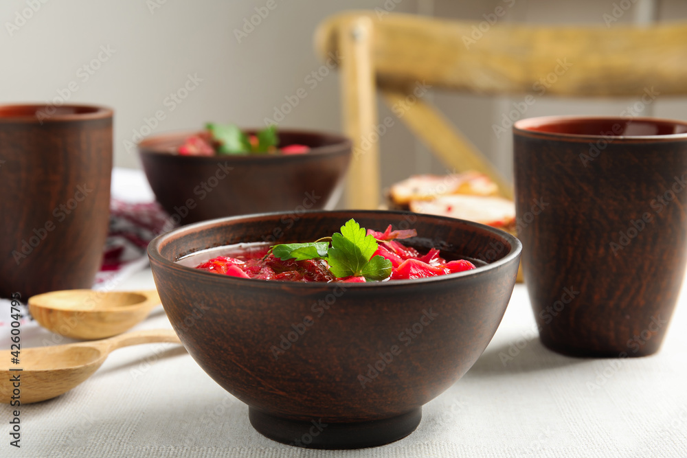 Stylish brown clay bowl with Ukrainian borsch served on white tablecloth Stylish brown clay bowl with Ukrainian borsch served on white tablecloth