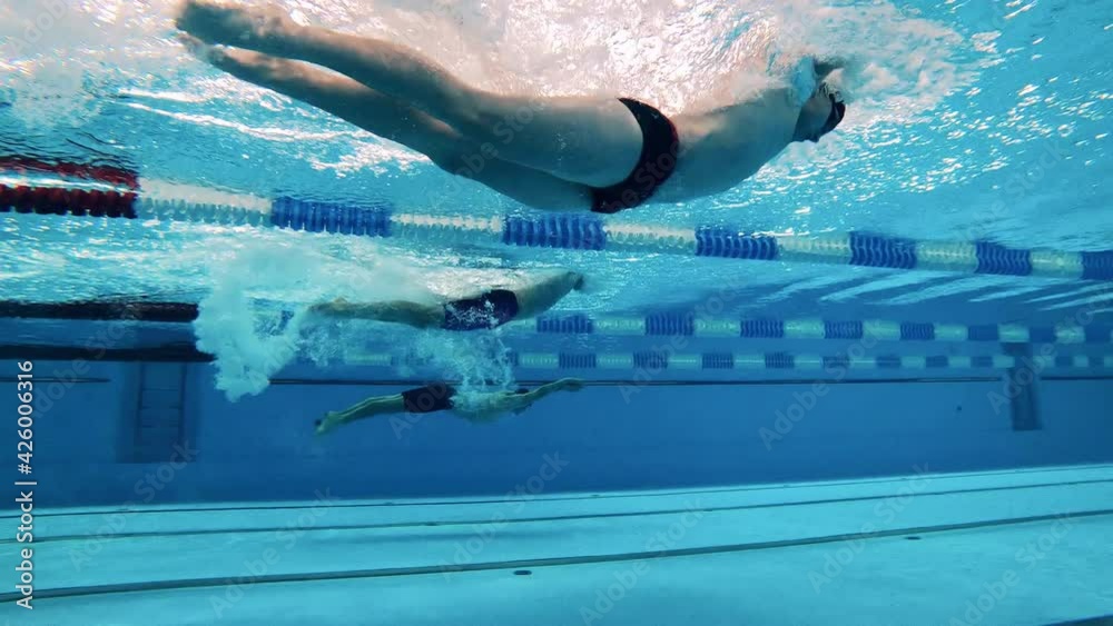 Three athletes swim underwater using dolphin kick technique