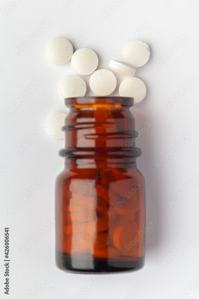 Macro Close up of medicinal or herbal white pill spilled and in an amber glass bottle. Top view, white background.