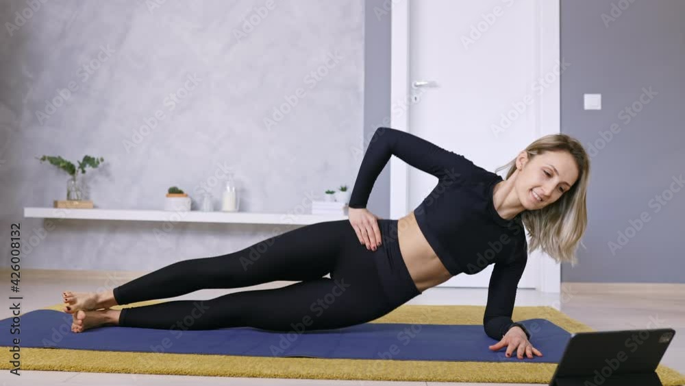 Woman Exercising at Home with Laptop or Smartphone watching online stream Fitness lessons and training in living room on mat wearing Workout Sport Outfit, Real Time, Copy Space Woman Exercising at Home with Laptop or Smartphone watching online stream Fitness lessons and training in living room on mat wearing Workout Sport Outfit, Real Time, Copy Space