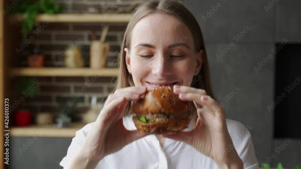 Hungry woman eating a hamburger sitting in the kitchen