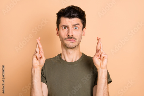 Photo of troubled nervous guy cross fingers look camera wear green t-shirt isolated beige color background
