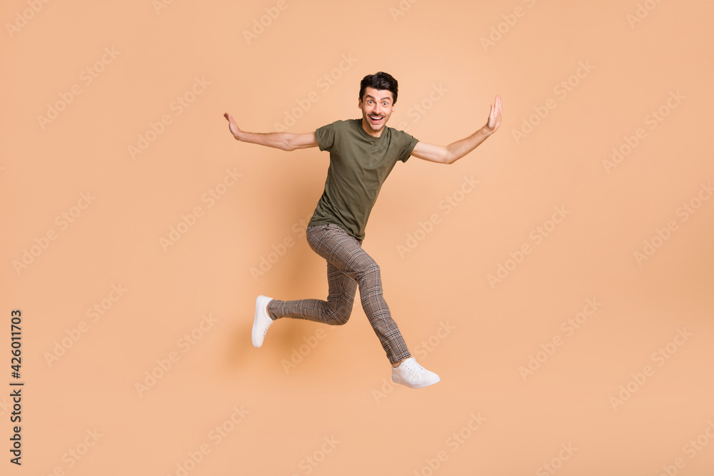 Full length body size photo of jumping high guy smiling wearing checkered pants t-shirt isolated on pastel beige color background