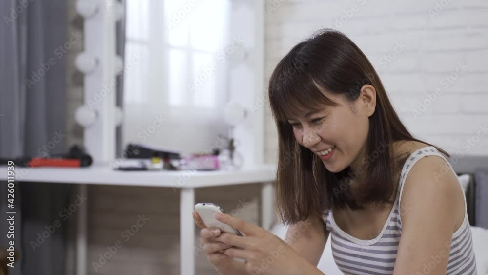 Japanese young lady in striped tank top using a cell phone. gorgeous female texting with her friends in the morning on the bed Japanese young lady in striped tank top using a cell phone. gorgeous female texting with her friends in the morning on the bed