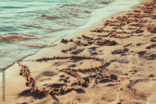 Drawing heart on the sand by the sea. Love symbol between man and woman