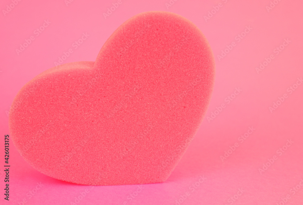 a washcloth, sponge in the shape of a pink heart on a pink background. Romantic background.