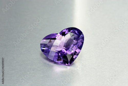Natural Bolivian deep purple amethyst gemstone. Heart checker faceted loose semiprecious violet color quartz gemstone setting. Gray metallic satin gradient background. 
