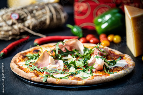 Delicious crispy pizza with prosciutto surrounded by salami and vegetables