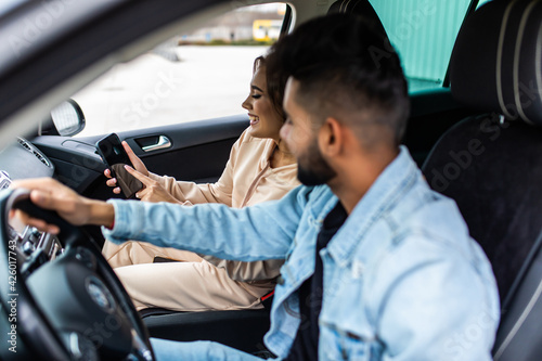 Young indian woman holds smart phone, uses online maps, shows to husband, try to find way, being lost in big city, drive car, have journey in strange country. 