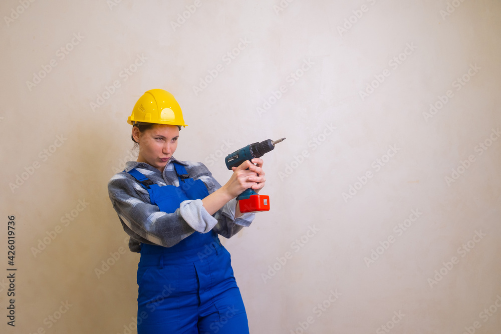 A beautiful brunette woman in a blue uniform and a yellow helmet holds a screwdriver and pretends to shoot a gun