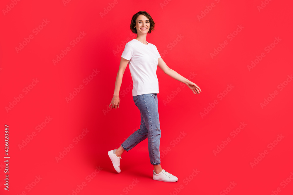 Full length body size profile side view of attractive glad content cheerful girl going isolated over bright red color background Full length body size profile side view of attractive glad content cheerful girl going isolated over bright red color background