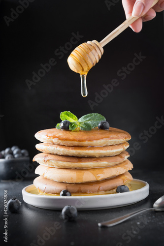 Homemade stack of pancakes with blueberry and honey on black background.