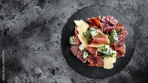 Antipasto board with sliced meat, ham, salami, cheese for red wine. raditional Spanish meat snacks on a slate board