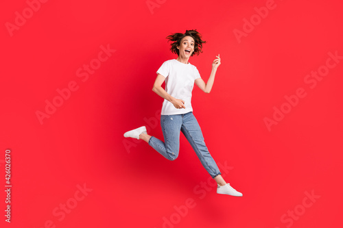 Full length body size view of attractive funny cheerful girl jumping playing invisible guitar having fun isolated over bright red color background