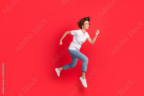 Full length body size view of attractive motivated cheerful girl jumping running fast isolated over bright red color background