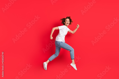 Full length body size profile side view of attractive cheerful girl jumping running isolated over bright red color background