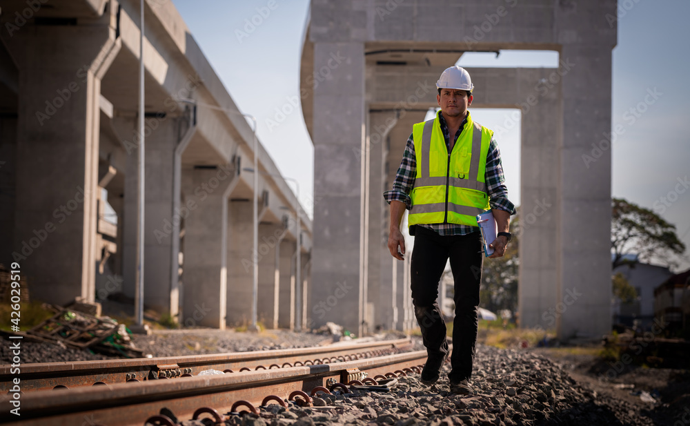 Engineer railway under inspection and checking construction process train and railroad station .Engineer wearing safety uniform and helmet by holding document in work.
