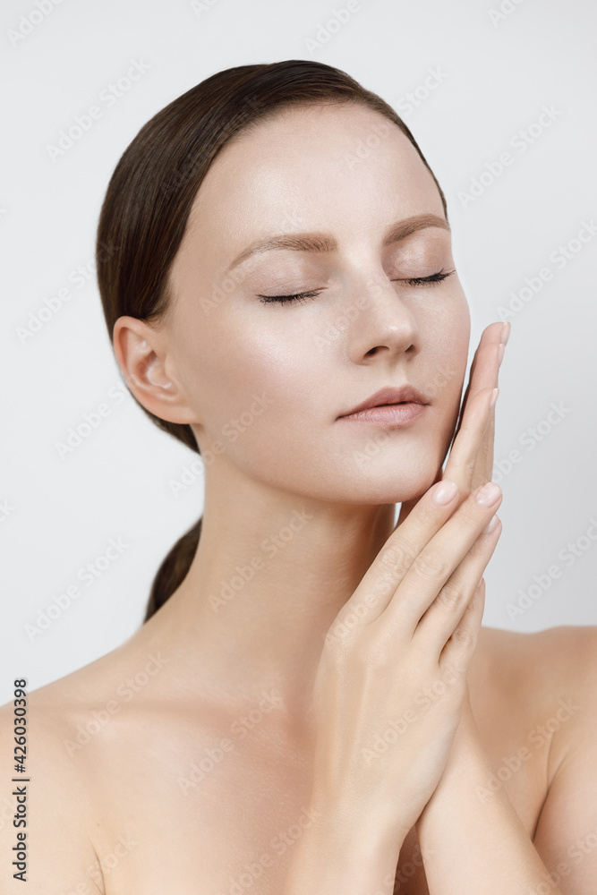Young woman with beautiful healthy face - isolated on white background, studio hi-end shot, skin care concept. Hands and fingers gently touch facial skin, brown hair parted, gathered in low ponytail Young woman with beautiful healthy face - isolated on white background, studio hi-end shot, skin care concept. Hands and fingers gently touch facial skin, brown hair parted, gathered in low ponytail