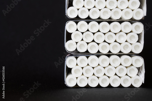 Many cigarettes with white filters, equipped with air chambers, lie in three packs against a dark background.  Free space for an inscription photo