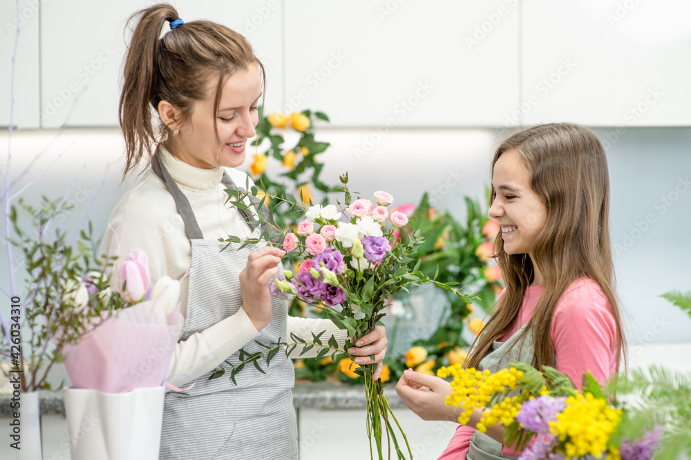 Woman teaches to young girl arranging flower at  floral shop