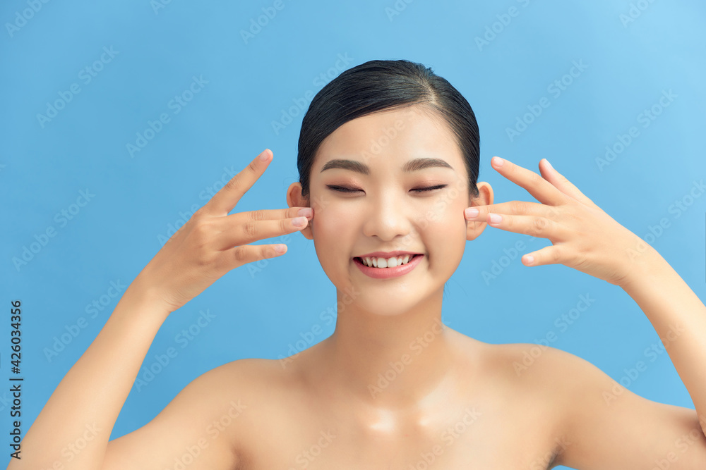 Beautiful smiling asian girl model with natural makeup touching glowing hydrated skin on blue background closeup Beautiful smiling asian girl model with natural makeup touching glowing hydrated skin on blue background closeup