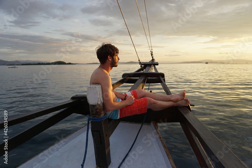 Junger Mann auf Schiff blickt in den Sonnenuntergang