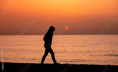 Silhouette of a woman walking by the ocean. Woman shilouette at sunrise on the beach © Robert
