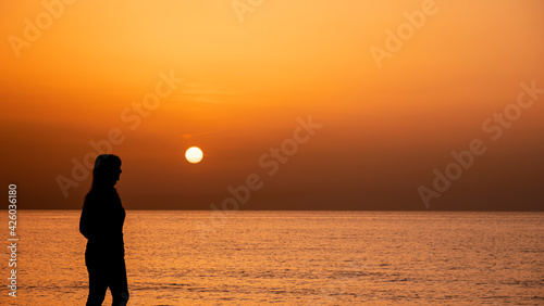 Silhouette of a woman walking by the ocean. Woman shilouette at sunrise on the beach