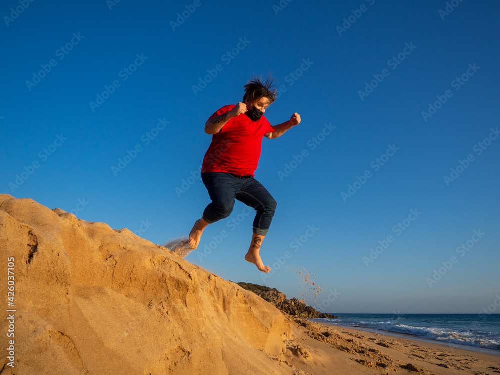 Hombre saltando con mascarilla en la playa