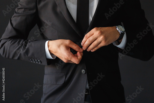 The groom fastens the button of his black jacket