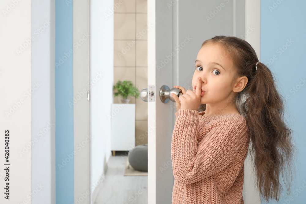 Cute little girl showing silence gesture near opened door Cute little girl showing silence gesture near opened door