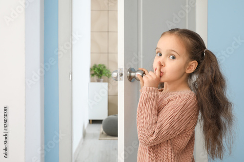 Cute little girl showing silence gesture near opened door