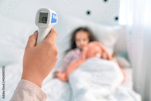 Woman measuring temperature of her little daughter ill with flu in bedroom