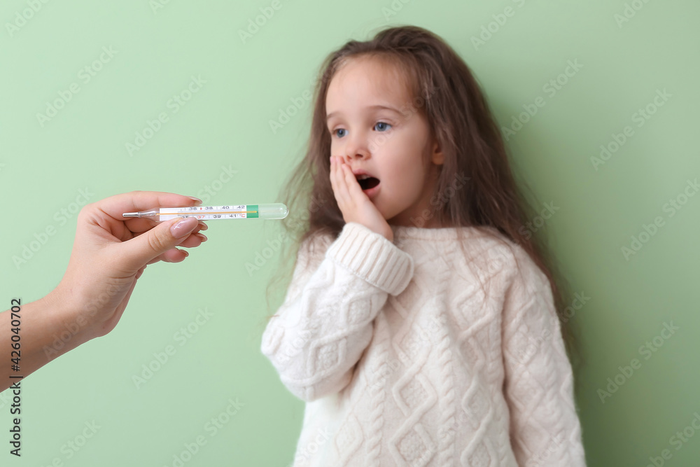 Woman measuring temperature of her little daughter ill with flu against color background Woman measuring temperature of her little daughter ill with flu against color background
