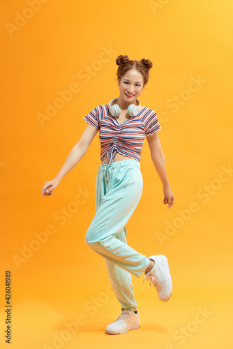 Portrait of girlish girl jumping in the air with raised leg isolated on yellow background