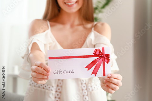 Beautiful young woman with gift card at home photo