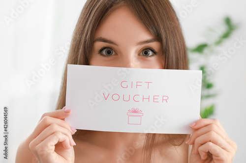 Beautiful young woman with gift voucher at home photo