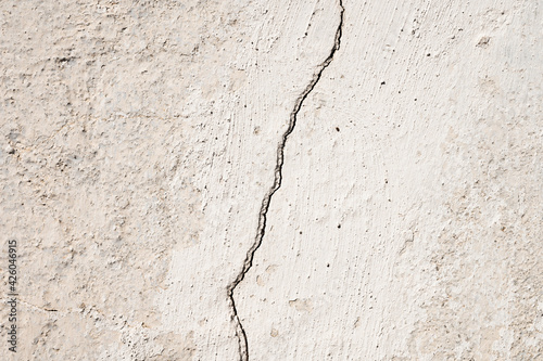 Grunge gray background of cracked peeling walls with peeled putty in beige tones.