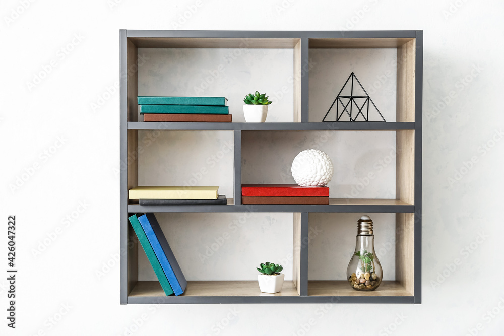 Shelf with books and decor hanging on light wall