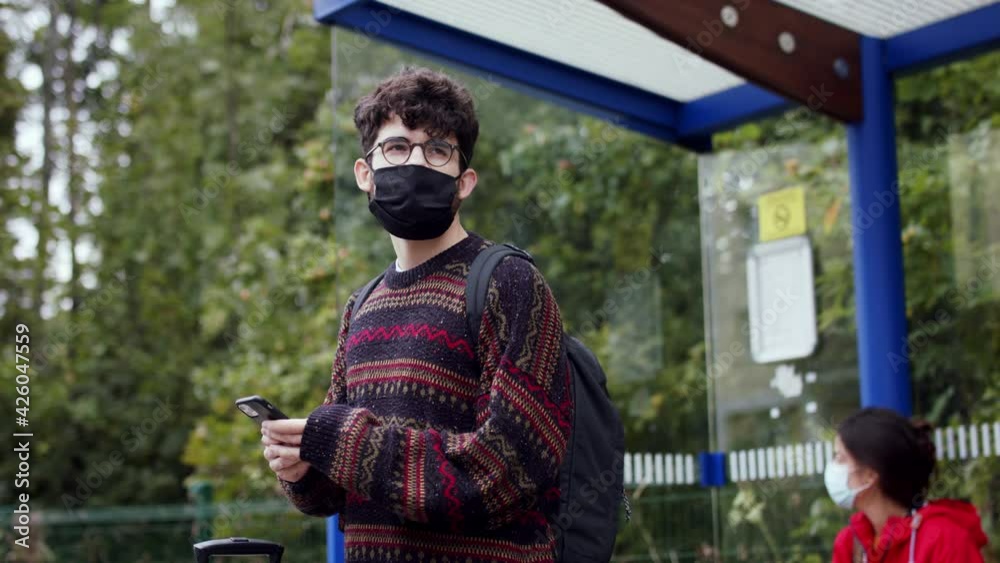 Young people with smartphone on bus stop outdoors in town, getting upset. Coronavirus concept.