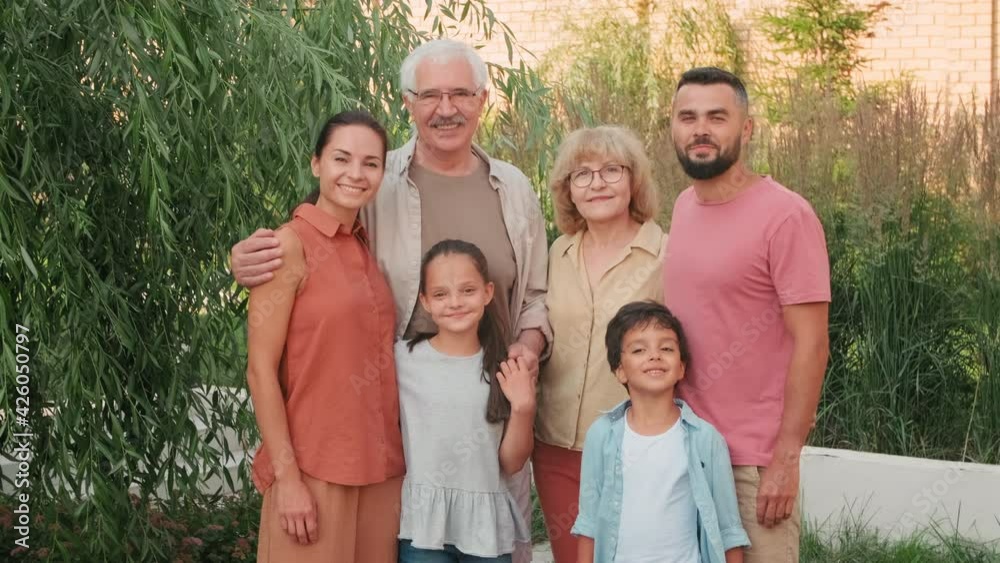 Medium portrait of cheerful multigenerational family of six standing outdoors on sunny summer day smiling to camera Medium portrait of cheerful multigenerational family of six standing outdoors on sunny summer day smiling to camera