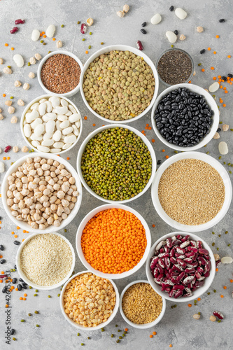 Mix of legumes, chickpeas, lentils, beans, peas, quinoa, sesame, chia, flax seeds in bowls on a gray concrete background. Top view.