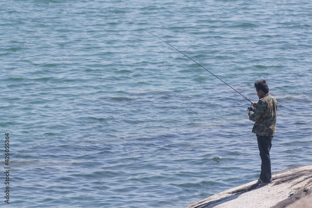Angler standing on rocks at Hua Hin Beach, Thailand - January 24,2021; Angler standing on rocks at Hua Hin Beach, Thailand - January 24,2021;
