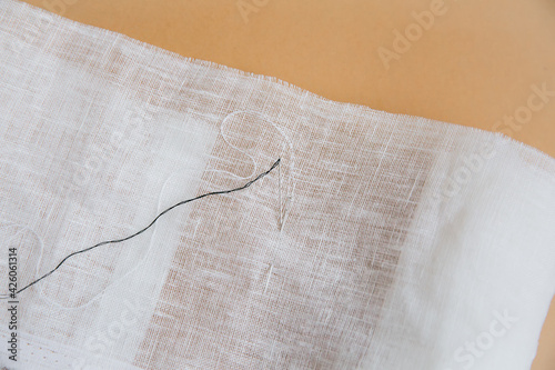 Sewing and needlework concept. Needles with black and white threads, natural fabric on a beige background.
