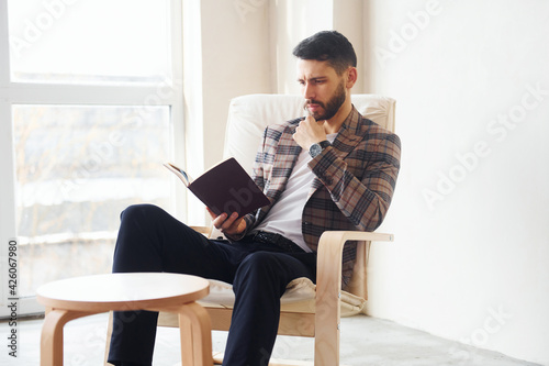 Reads book. Young stylish businessman in suit indoors. Conception of success