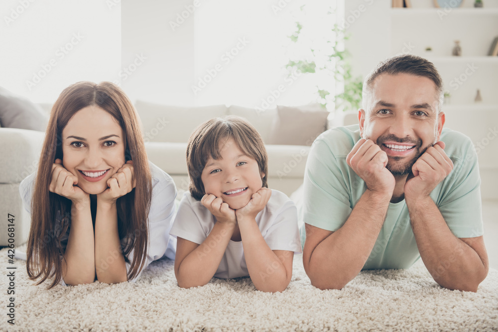 Photo of optimistic nice family mom dad kid hands face lie on floor wear t-shirts at home Photo of optimistic nice family mom dad kid hands face lie on floor wear t-shirts at home